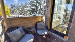 A balcony with two wicker chairs and a small table, overlooking a snowy landscape with trees. - Powder Pointe by AvantStay | Minutes From Base Village (Park City)