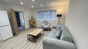 A modern living room with a grey sofa, a wooden coffee table, a white armchair, and a floor lamp. - A newly built 2023 apartment (Oxford)