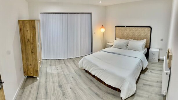 A hotel room with a large bed, a wooden wardrobe, a nightstand with a lamp, and a sliding door. - A newly built 2023 apartment (Oxford)