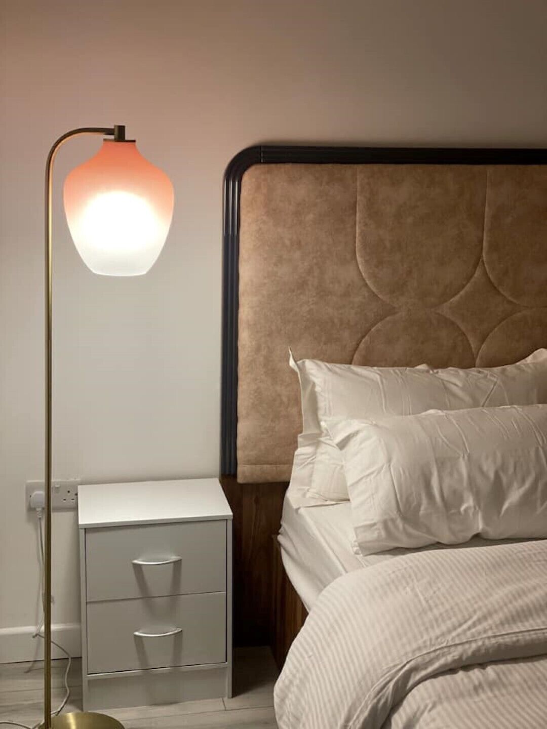 A bedroom with a bed, a bedside table with drawers, and a floor lamp.