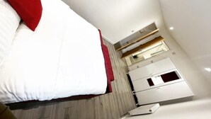 Une chambre d’hôtel moderne avec un lit, un oreiller rouge, un plancher en bois et une kitchenette dotée d’une fenêtre.