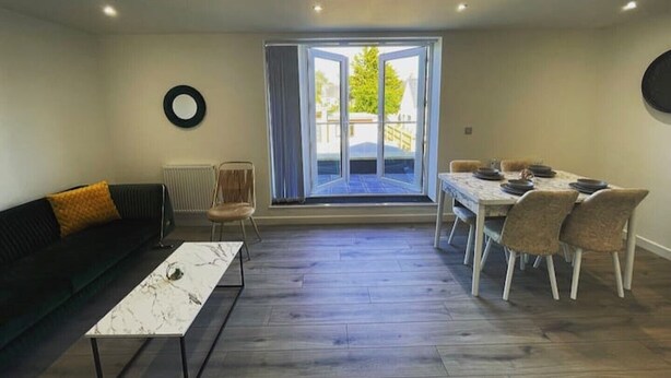 Un vaste espace de vie comprenant un canapé, une table à manger avec des chaises, une table basse et une grande porte-fenêtre coulissante donnant sur un balcon.