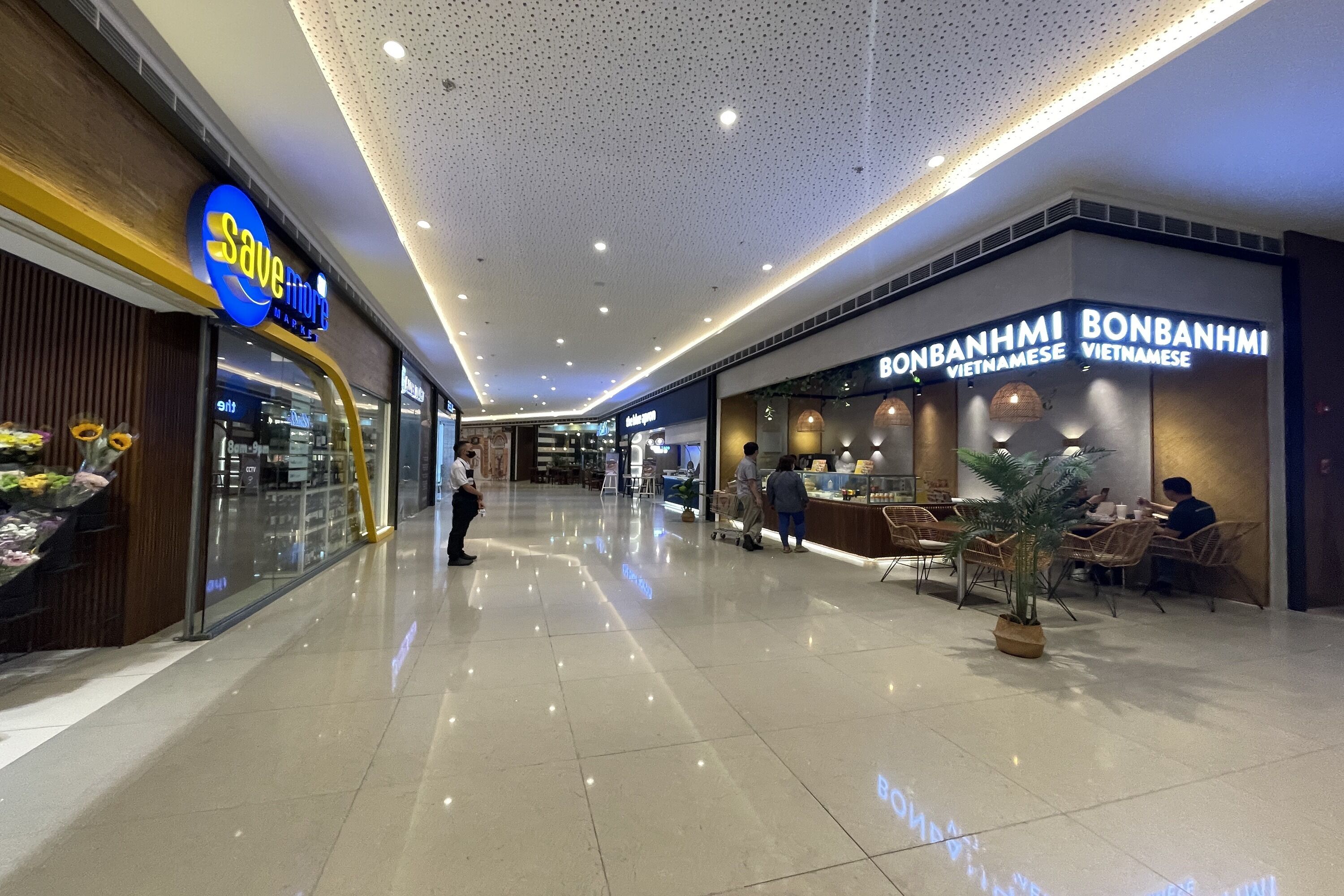 A modern shopping mall interior with a 'Save More' store and a 'Bonanham Vietnamese' restaurant.