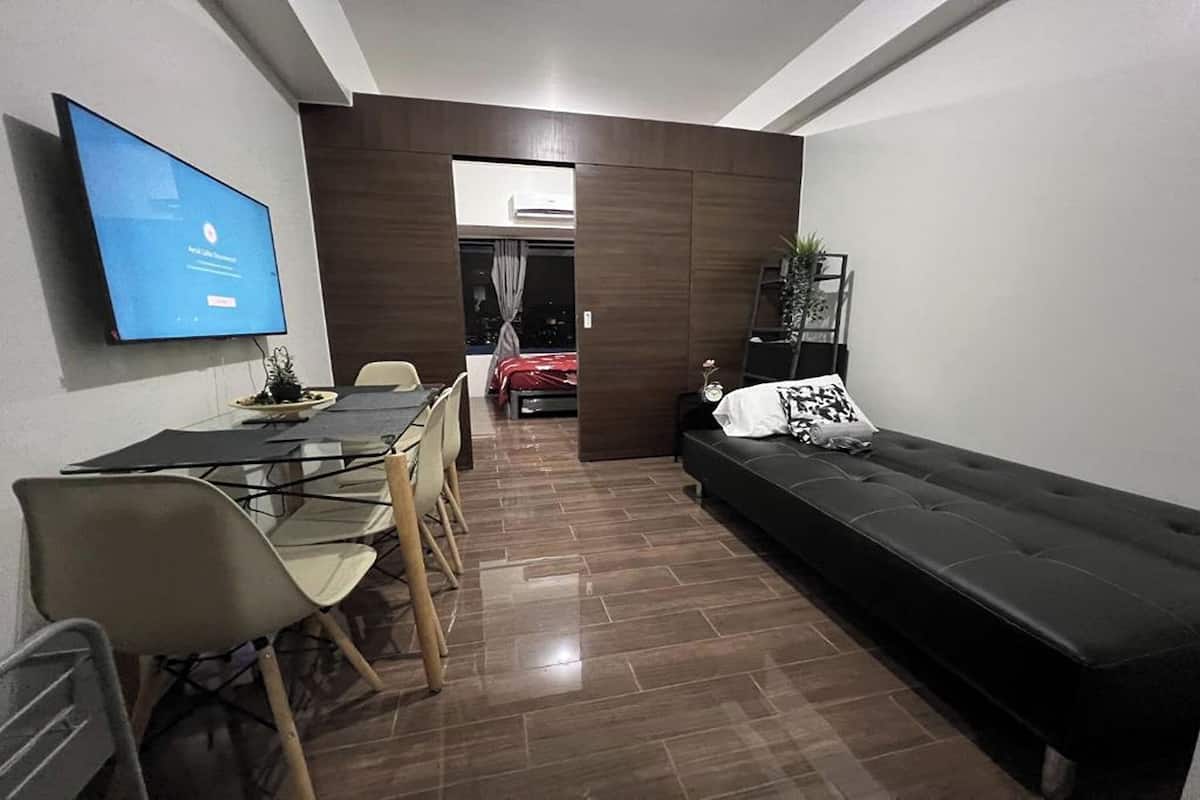 Un salon moderne avec un canapé noir, une table à manger avec des chaises et un téléviseur fixé au mur.