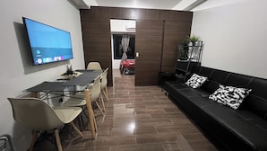Een moderne woonkamer met een televisie, eettafel en zwarte leren bank.