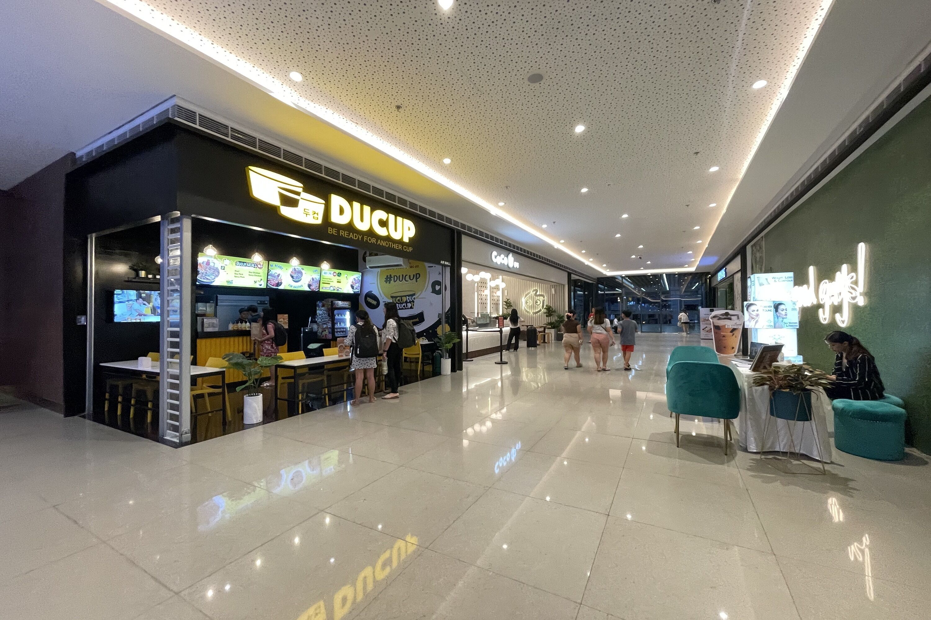A modern indoor shopping area with a food court featuring a DUCUP restaurant.