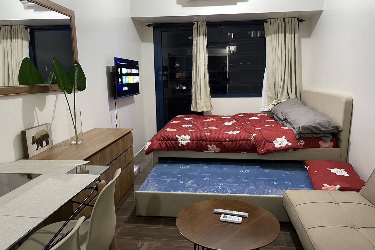 Une petite pièce comprenant un lit, une petite table, une chaise, un téléviseur et une fenêtre avec des rideaux.