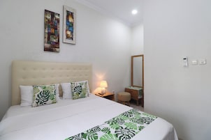 A hotel room with a large bed, a bedside table with a lamp, a mirror, and two paintings on the wall.