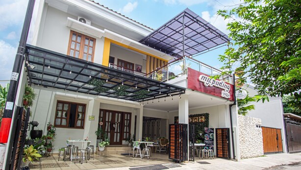 A two-story building with a covered patio area, outdoor seating, and a sign for a restaurant. - Bisma Balcony Homestay (Pogung Lor)
