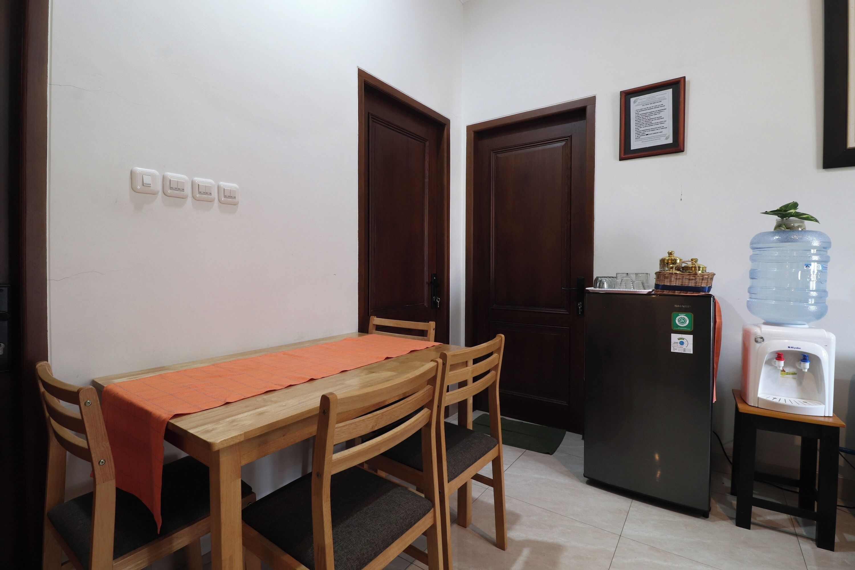 A small dining area with a wooden table and chairs, a water dispenser, and a refrigerator.