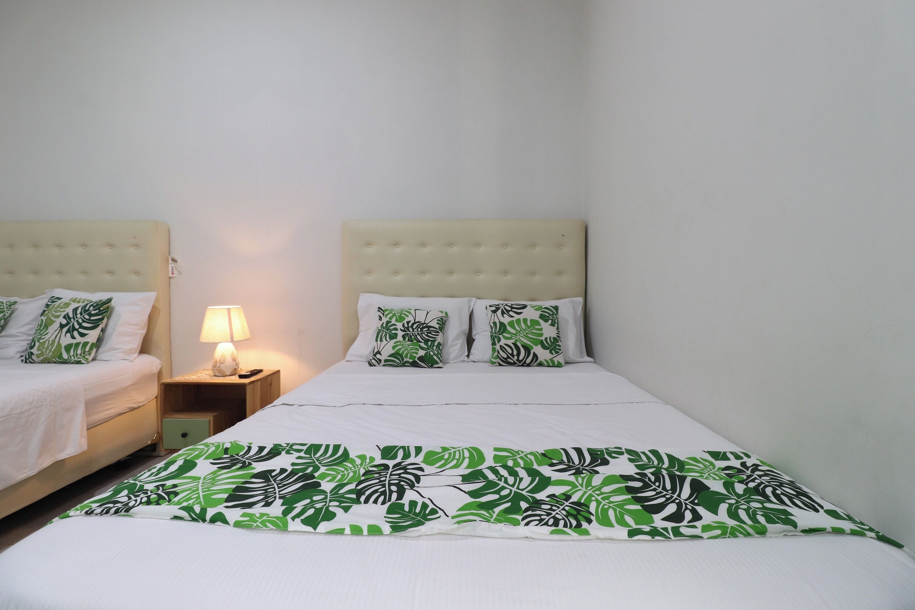 Una cama doble con edredón estampado en hojas verdes, dos mesitas de noche con lámparas y almohadas a juego.