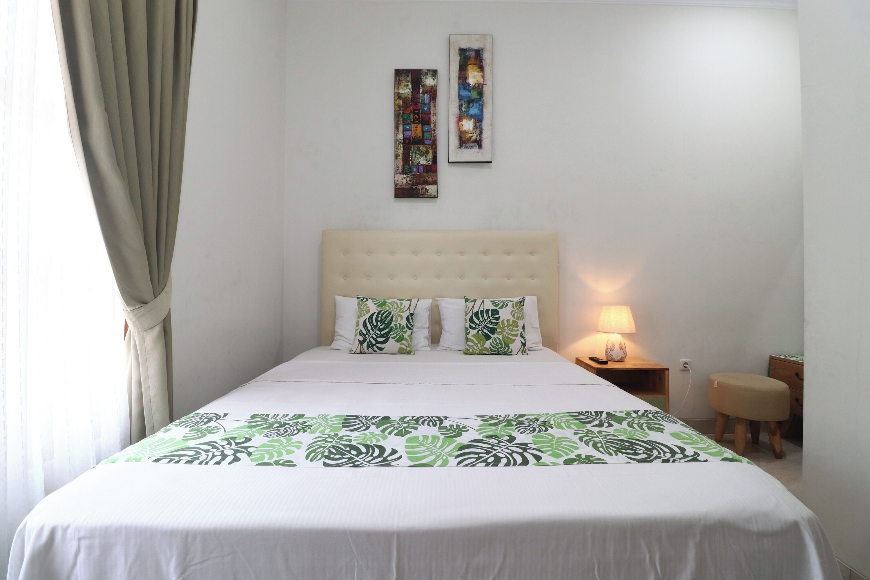 A neatly made bed with a green leaf pattern bedspread, a tufted headboard, and two wall-mounted artworks.
