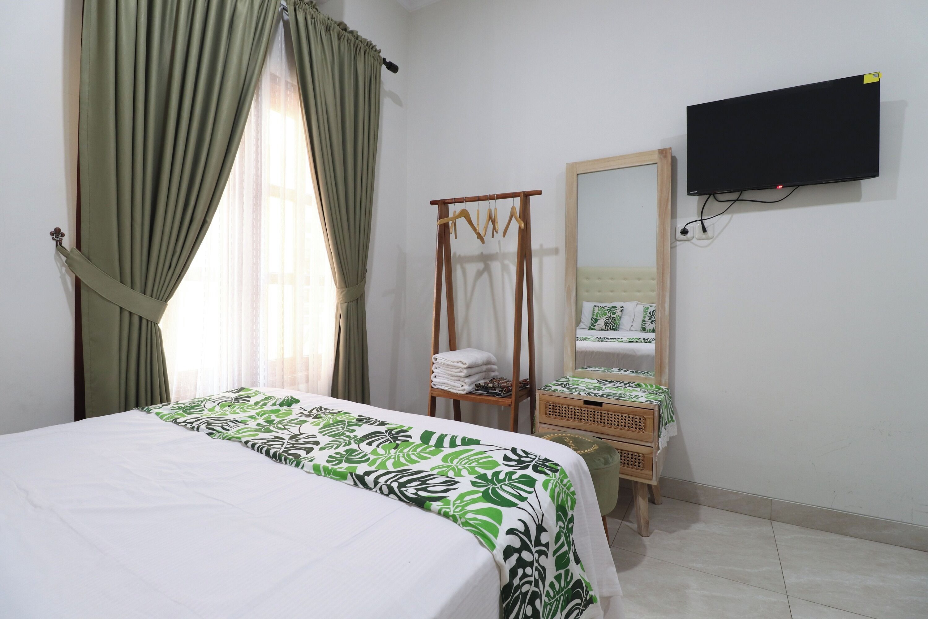 A hotel room with a bed, a wooden hanger, a mirror, and a television on the wall.