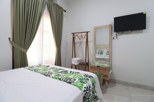 Una habitación de hotel con una cama, un perchero de madera, un espejo y un televisor en la pared.