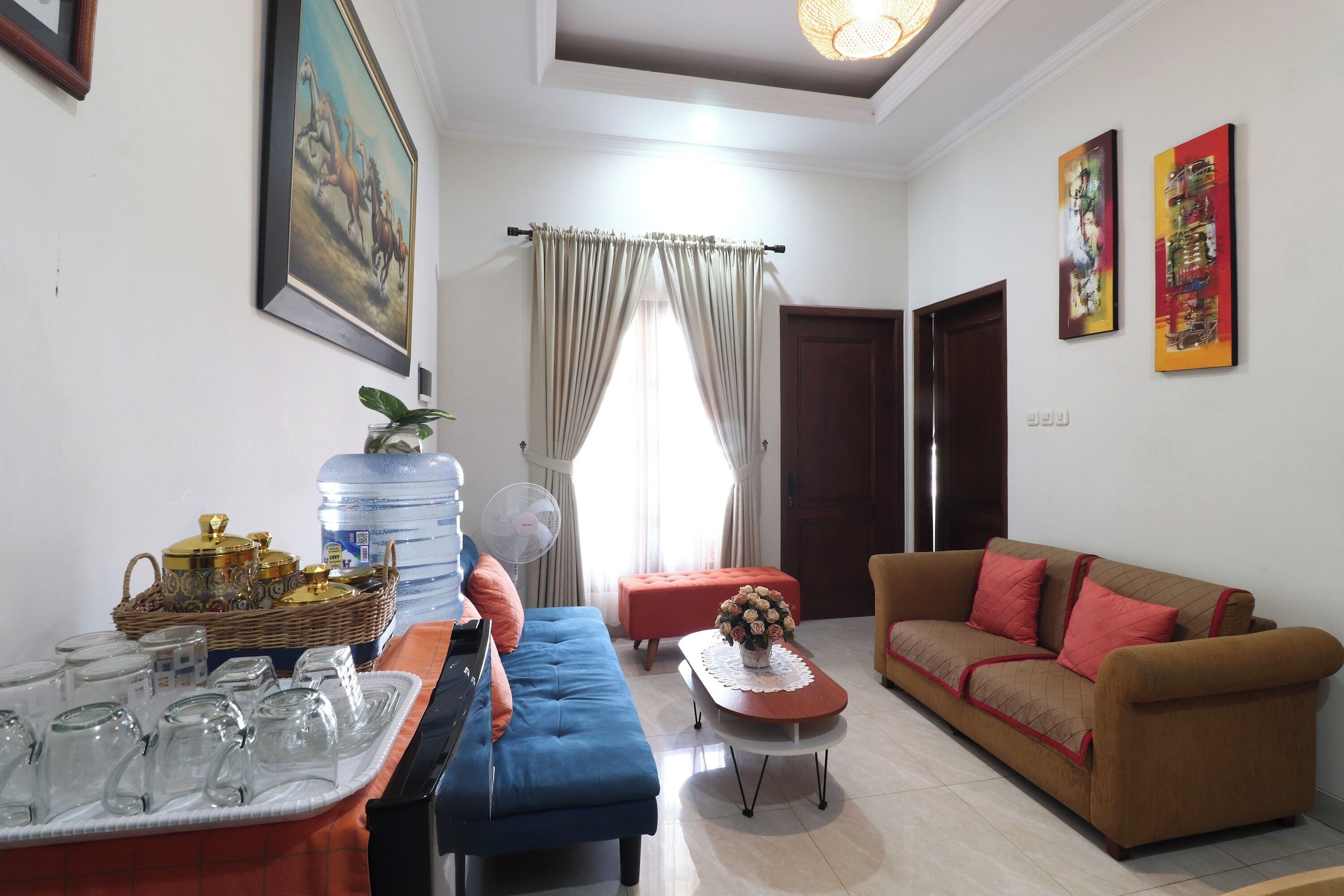 A living room with a sofa, a table with glasses, a water dispenser, and a painting on the wall.