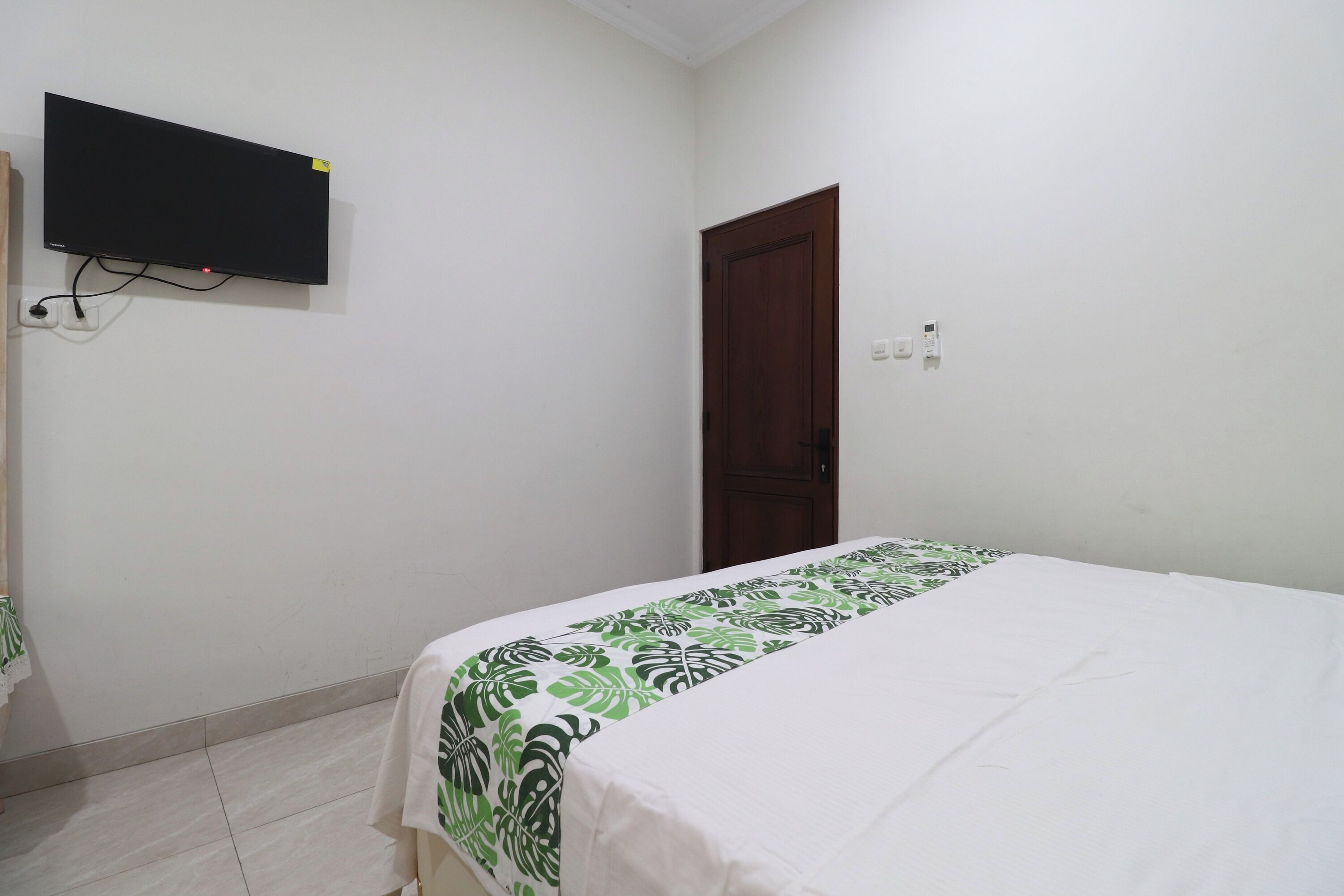 A bedroom with a bed, a television mounted on the wall, a door, and a wall socket.