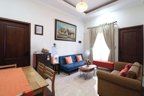 A living room with a dining area, a water dispenser, a sofa, a coffee table, and a large window with curtains. - Bisma Balcony Homestay (Pogung Lor)
