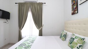 A hotel room with a bed, curtains, a television, and a wall-mounted air conditioner. - Bisma Balcony Homestay (Pogung Lor)