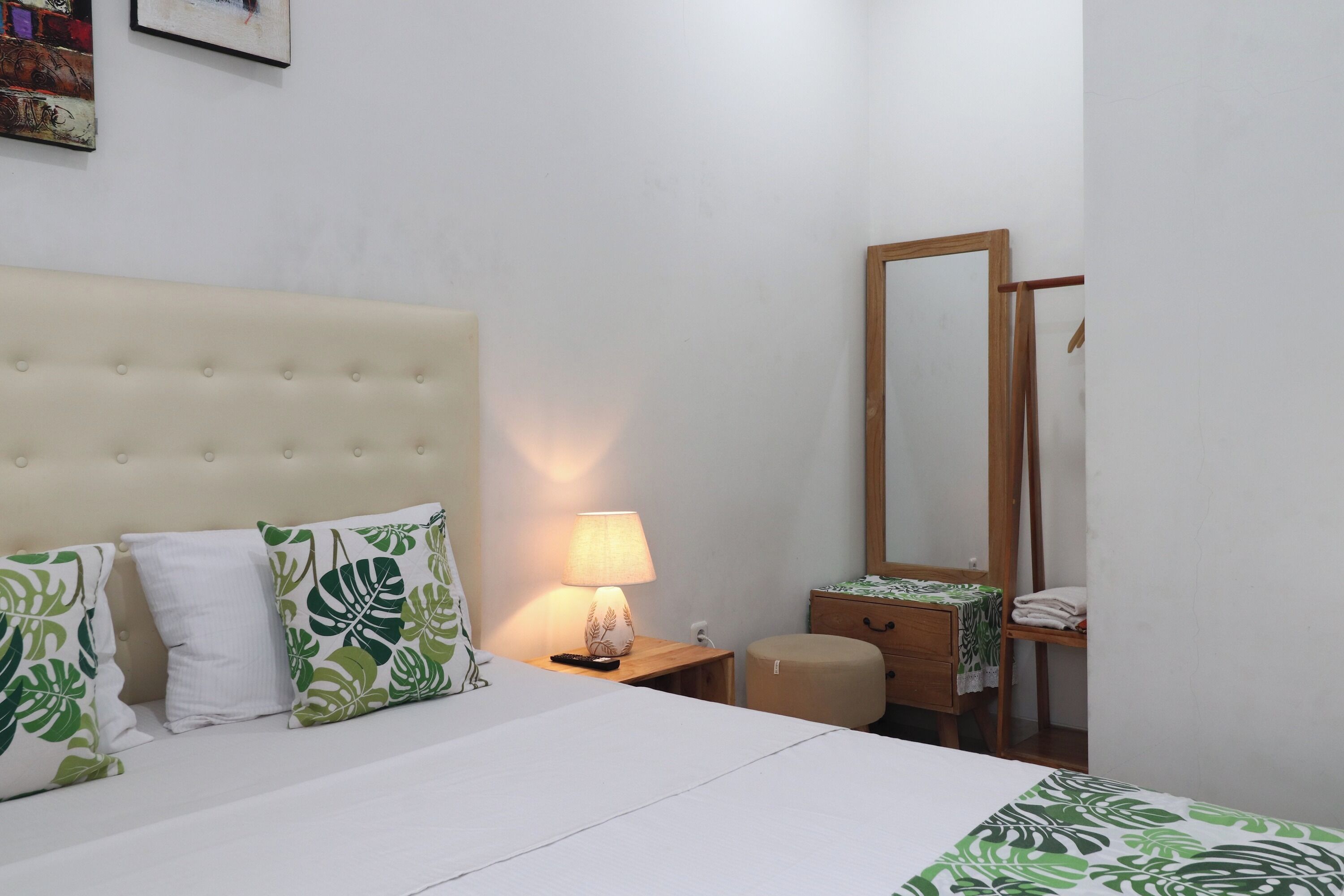 Une chambre d’hôtel avec un lit, une lampe de chevet, une table de chevet en bois, un miroir et un petit tabouret en bois.
