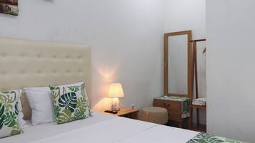 Une chambre d’hôtel avec un lit, une lampe de chevet, une table de chevet en bois, un miroir et un petit tabouret en bois.