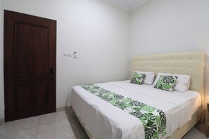 A bedroom with a large bed, a wooden door, and a white wall. - Bisma Balcony Homestay (Pogung Lor)
