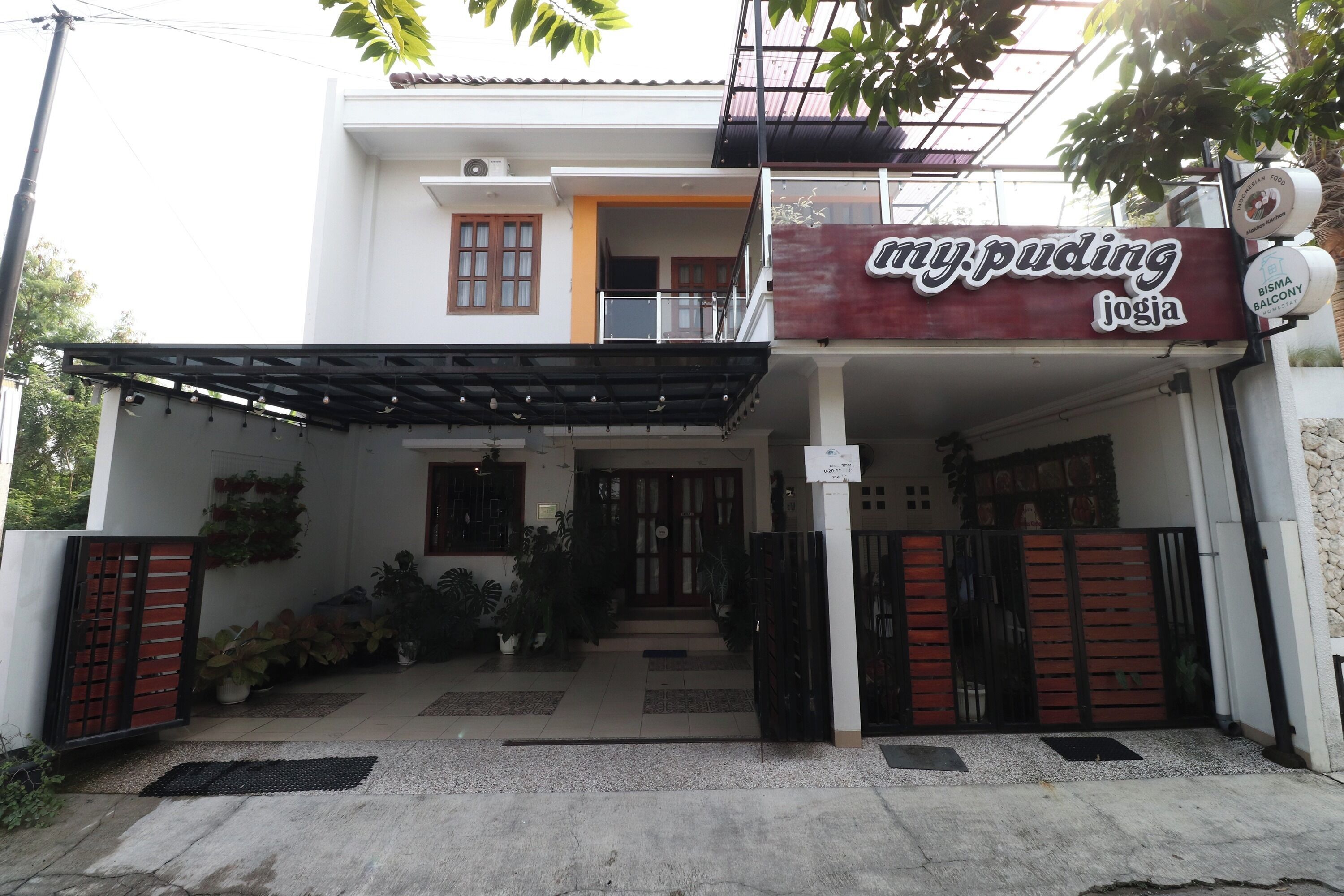 A two-story building with a covered entrance, a sign for 'my.puding joga', and a gated driveway.