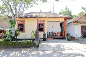 Una casa tradicional con techo de tejas, un porche delantero y un pequeño jardín con plantas y un árbol.
