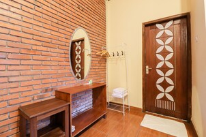 Un baño con pared de ladrillo, tocador de madera, espejo, toallero y puerta con diseño geométrico.