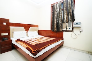 A neatly made bed with a patterned blanket, a wooden headboard, a bedside table with a phone, and an air conditioning unit on the wall.