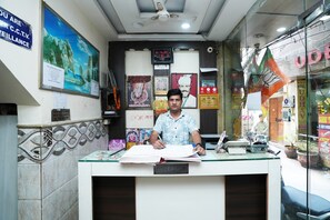 A reception desk with a man writing at it, surrounded by various posters and a clock.