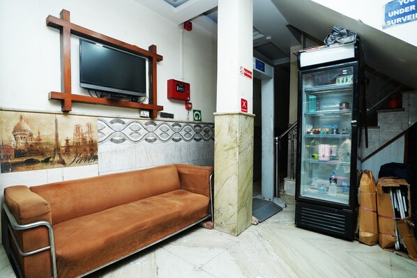A room with a sofa, a television mounted on the wall, a refrigerator, and a tiled wall with a Paris-themed mural.