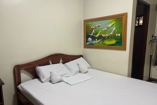 A neatly made bed with white linens and pillows, a wooden headboard, and a framed painting of fish on the wall.