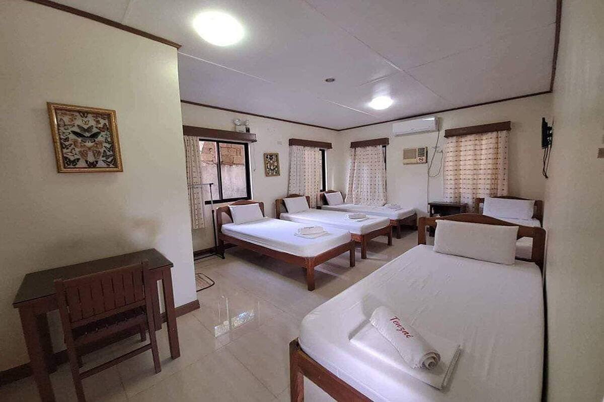 Una habitación de hotel con tres camas individuales, un escritorio de madera y una mesita pequeña.