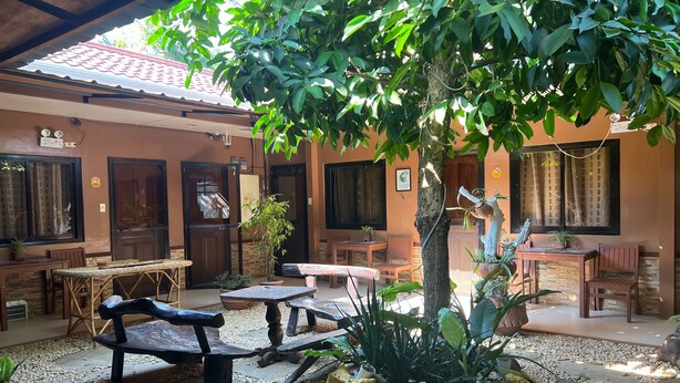 A covered outdoor seating area with tables and benches, surrounded by potted plants and a tree. - Tenzai Homestay (Puerto Princesa)