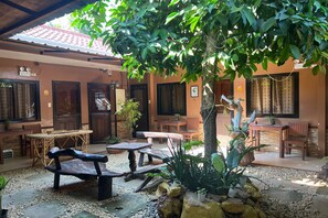 A covered outdoor seating area with tables and benches, surrounded by potted plants and a tree. - Tenzai Homestay (Puerto Princesa)