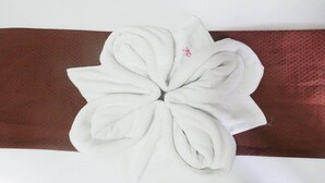 A white towel with a pink logo, placed on a brown fabric. - Tenzai Homestay (Puerto Princesa)