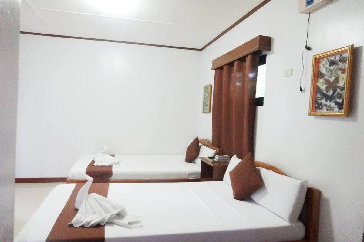 Habitación de hotel con dos camas, un cabecero de madera, una mesita pequeña y una obra de arte con una mariposa enmarcada en la pared.