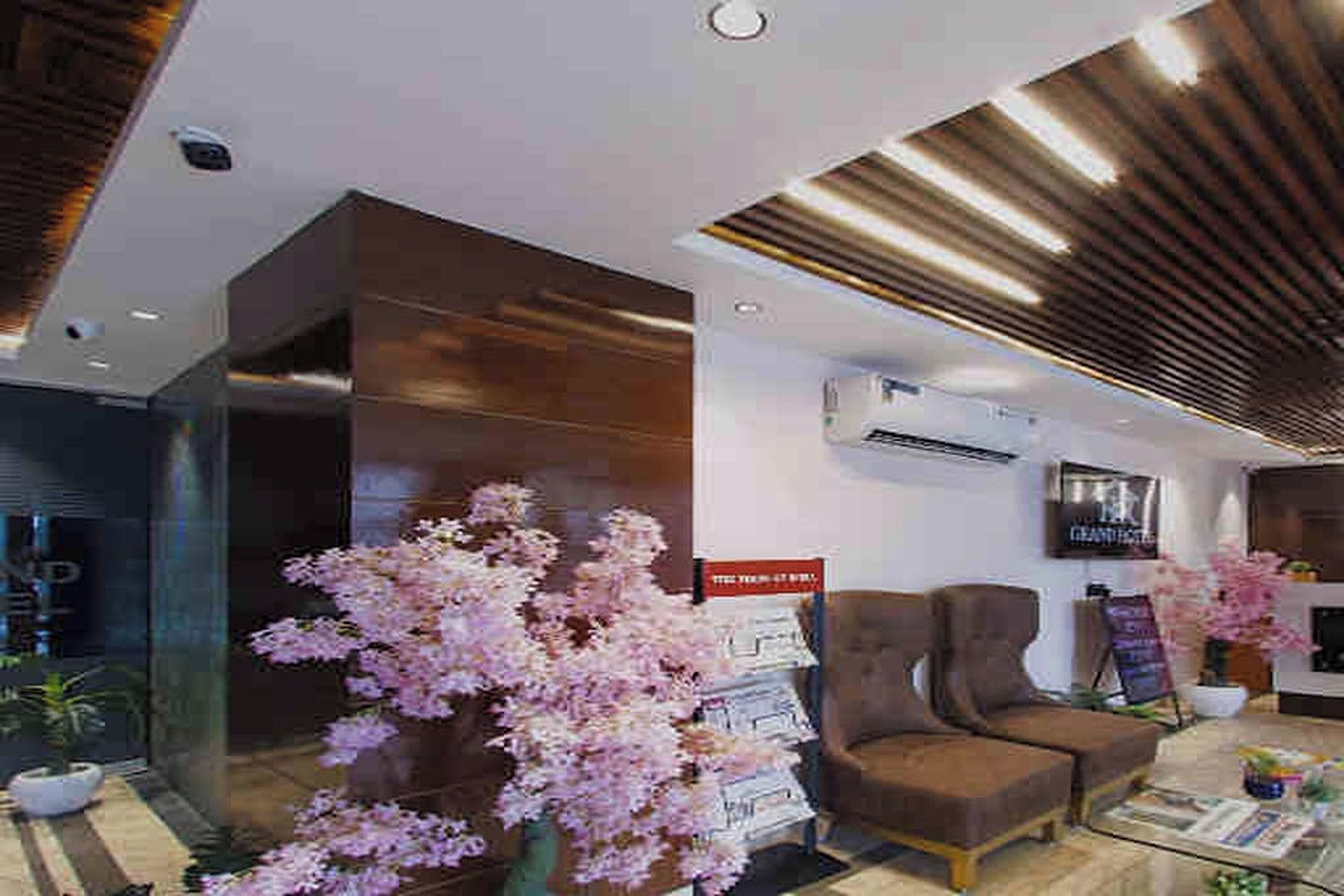 A modern lobby with a wooden ceiling, a seating area with two sofas, a coffee table, and a large pink flower arrangement.