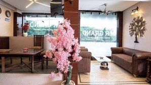 Un vestíbul d'hotel modern amb zona de dinar, un sofà, un arbre decoratiu i una finestra gran amb vistes.