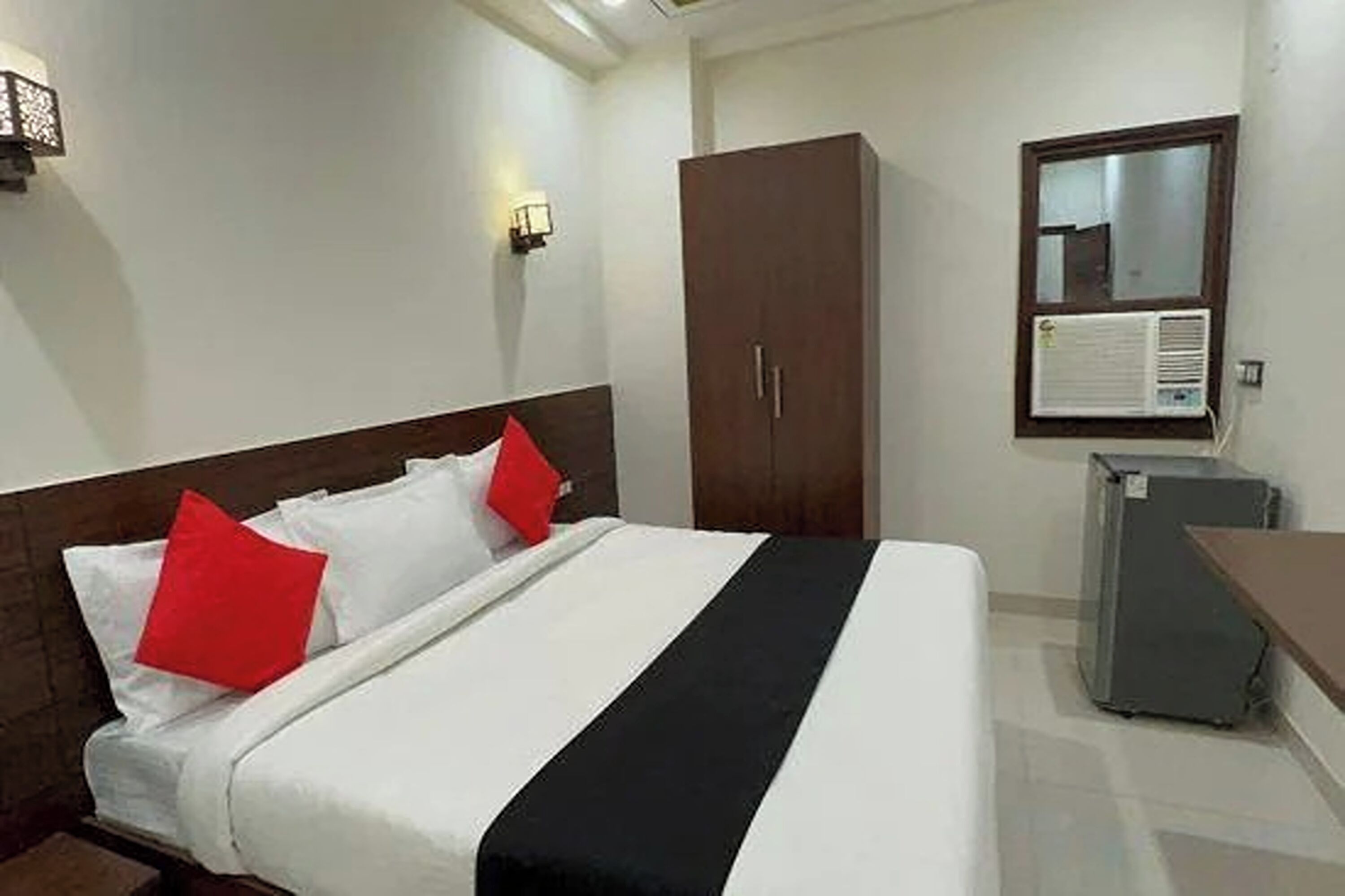 A hotel room with a bed, a wardrobe, a desk, and an air conditioning unit.