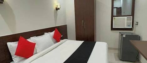 A hotel room with a bed, a wardrobe, a desk, and an air conditioning unit.