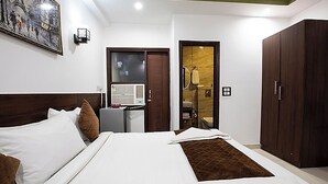 Habitació d'hotel amb un llit gran, una taula de treball amb un ordinador, un armari i un bany visible a través d'una porta de vidre.