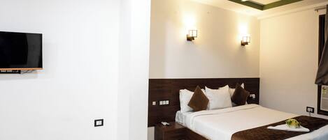 A hotel room with a large bed, a flat-screen TV mounted on the wall, and two wall-mounted lights.