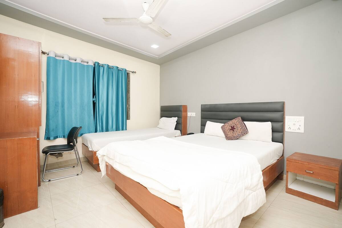 A hotel room with two beds, a wooden wardrobe, a desk, and a chair.