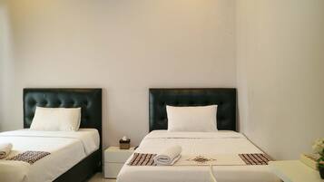 A hotel room with two beds, each with a black headboard and white bedding. There is a small bedside table with a tissue box and a rolled towel on each bed.