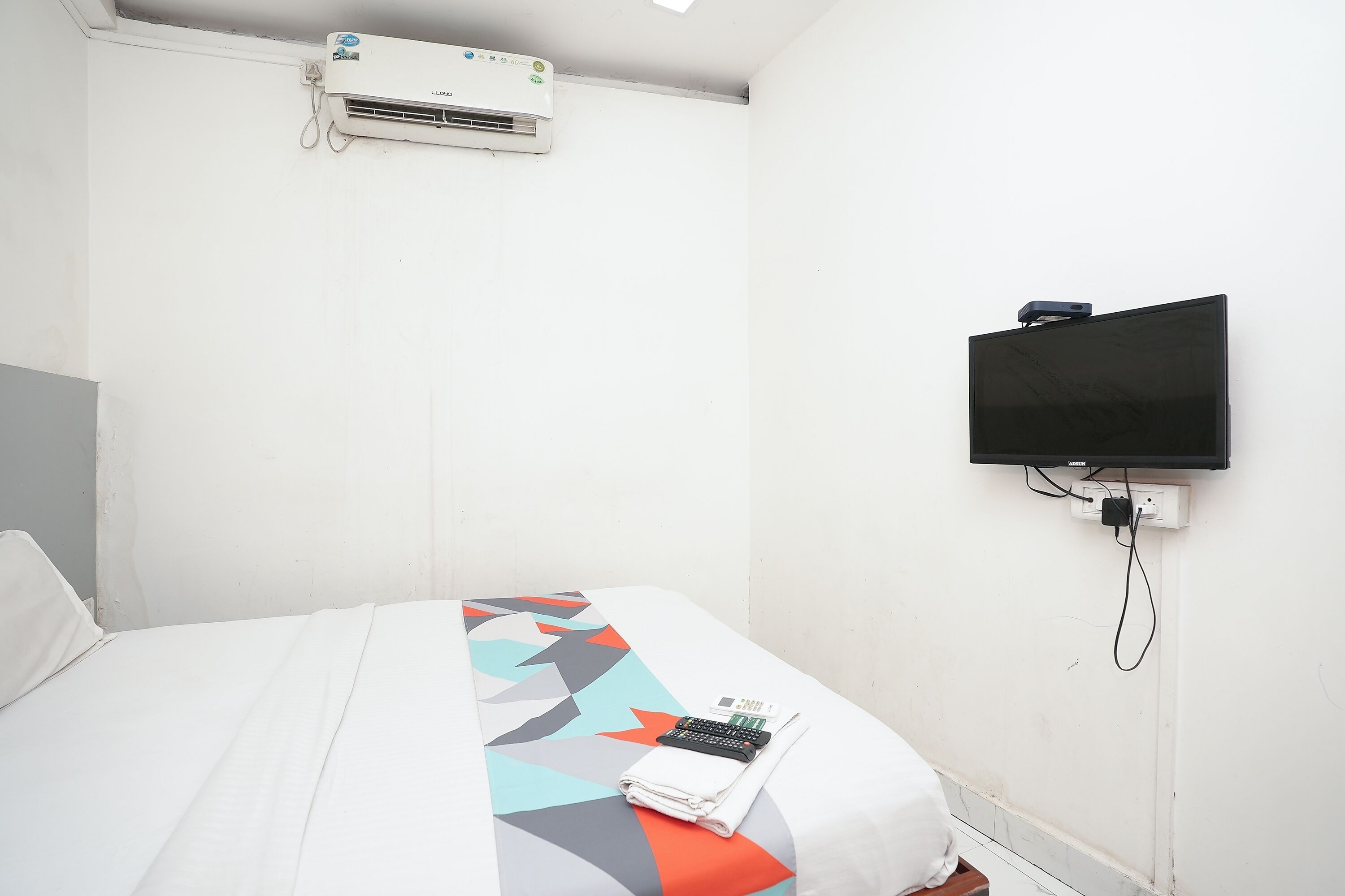 Ett hotellrum med en säng, en tv som är monterad på väggen och en luftkonditioneringsanläggning ovanför sängen.