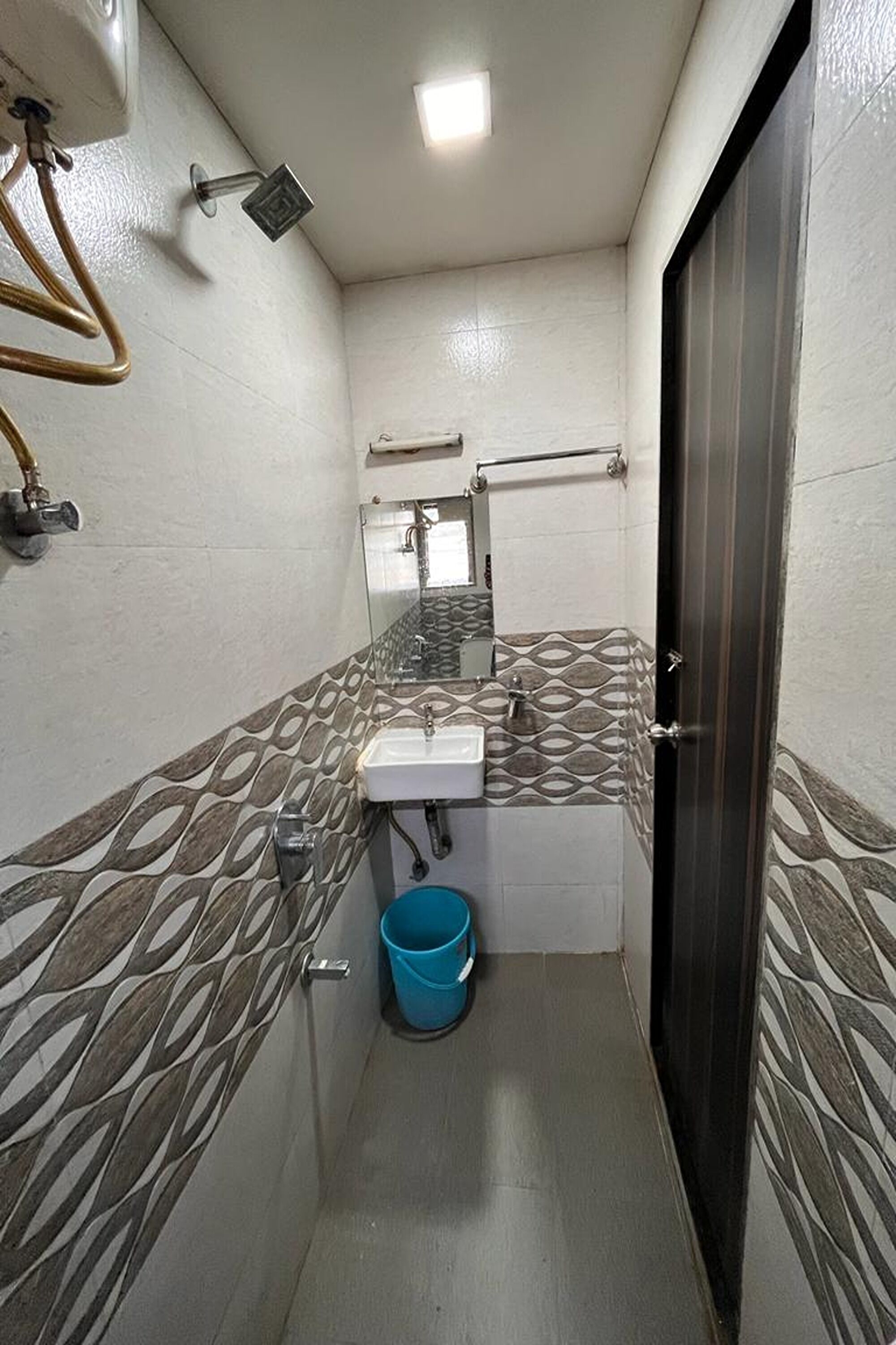 Ein schmales Badezimmer mit gemusterten Wänden, einem weißen Waschbecken, einem Spiegel und einem blauen Eimer.