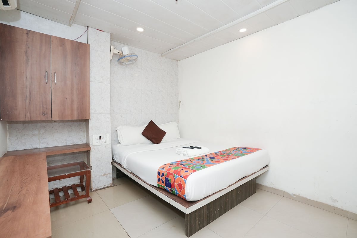 Une chambre à coucher avec un lit, un bureau en bois, un ventilateur fixé au mur et un plafond blanc.