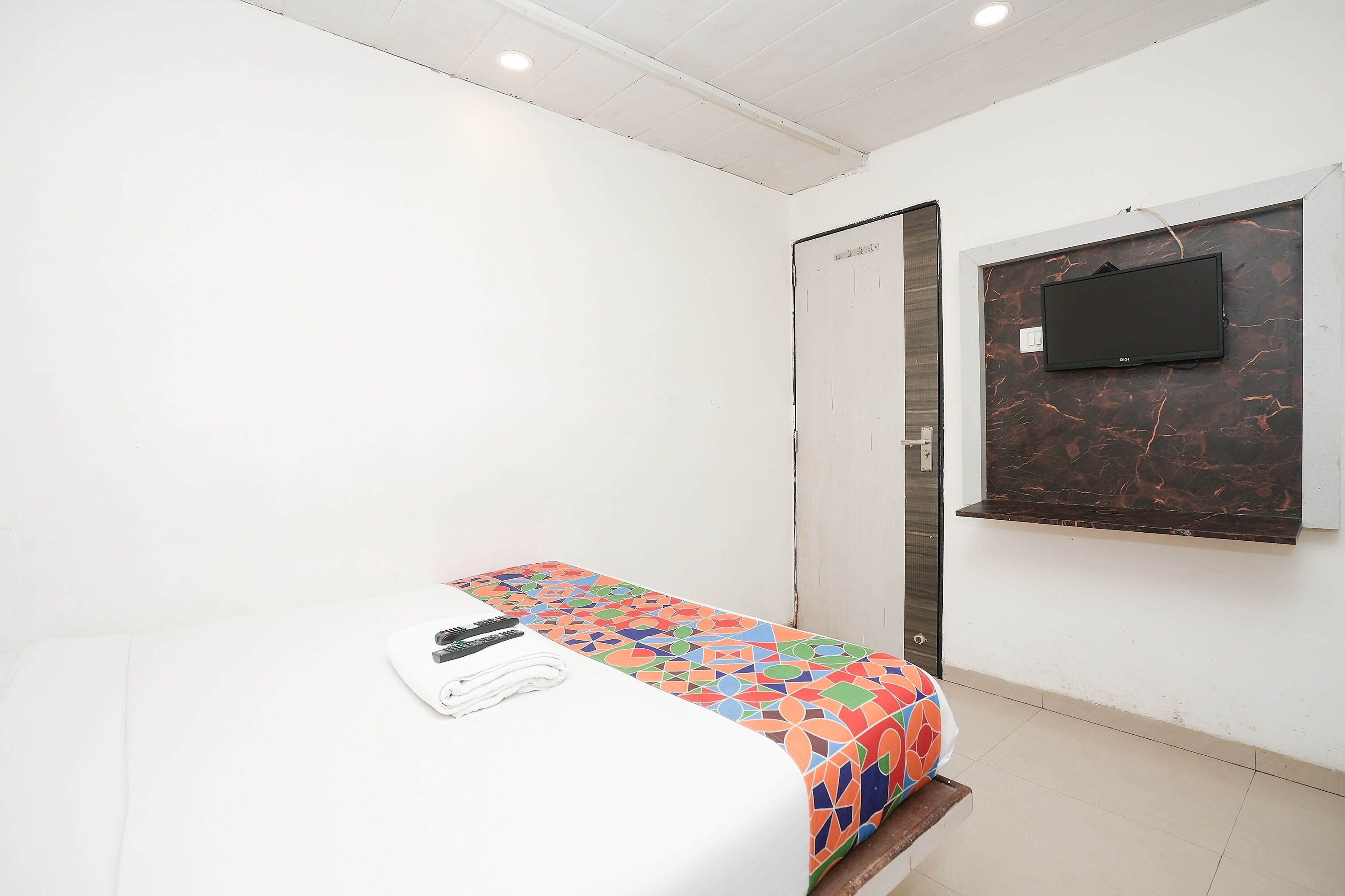 A small, clean room with a bed, a TV mounted on the wall, and a door.