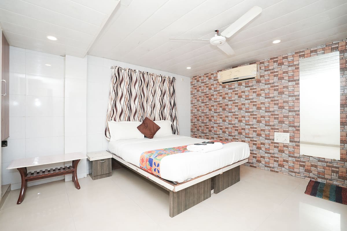 Une chambre à coucher comprenant un lit, une table de chevet, un banc, un ventilateur de plafond et un mur décoré d’un motif en briques.